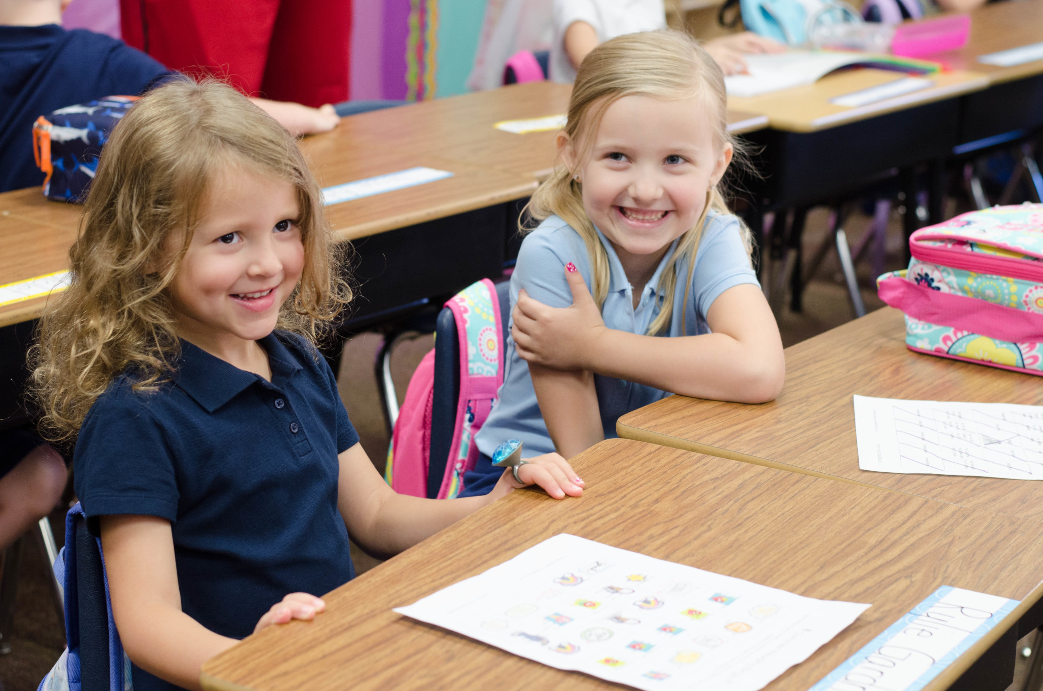 Two young elementary girls smiling in class at their desks