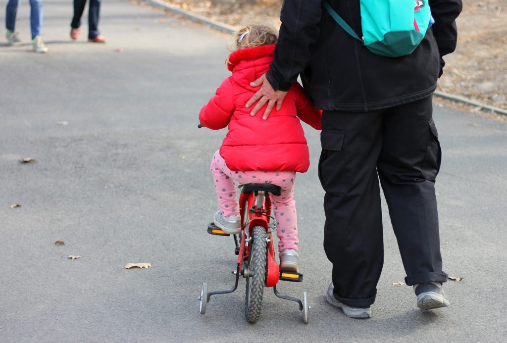 Father helps push his daughter on a bike with training wheels