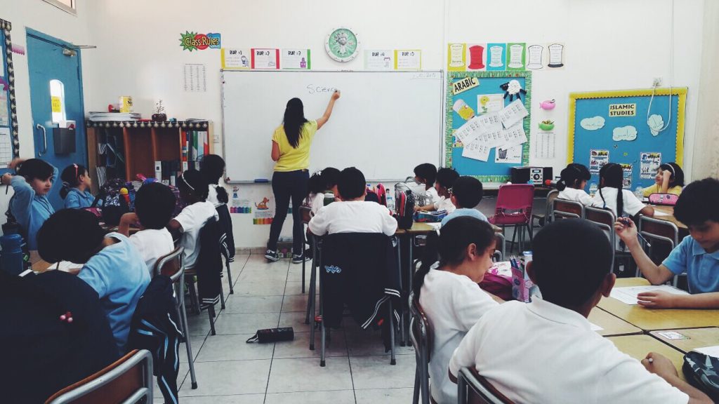 Teacher writing on a whiteboard in front of a class